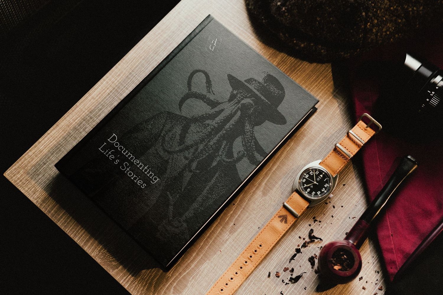 A leather notebook with embossed design lies beside a vintage watch with brown leather strap on textured surface.