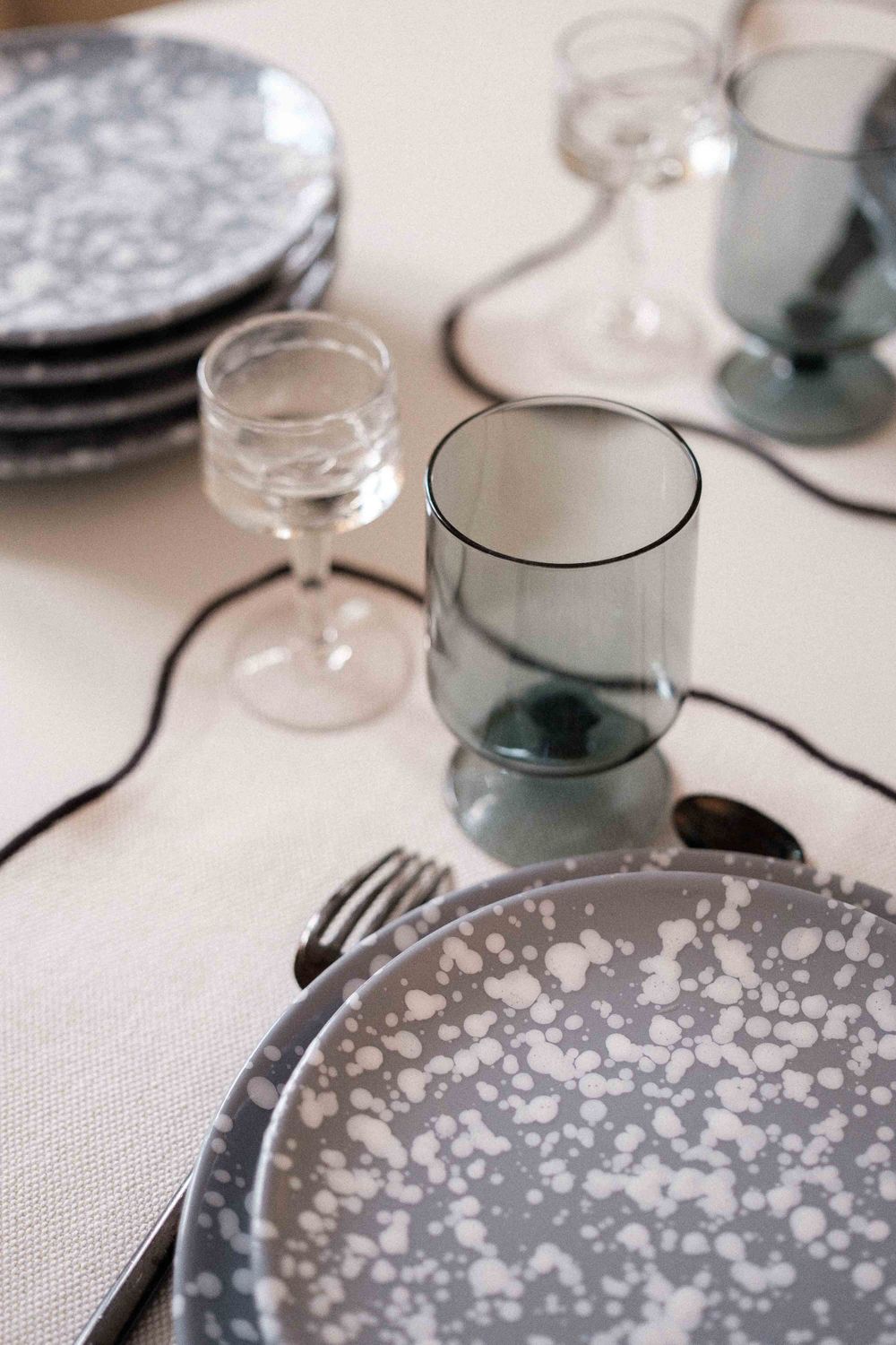 Table setting with speckled plates, smoky glassware, and minimalist place settings.