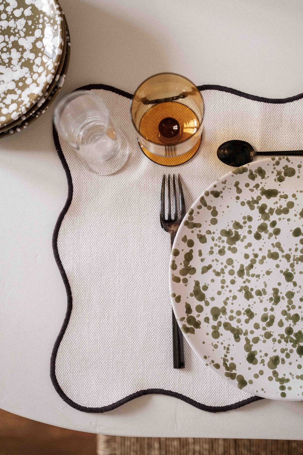 Place setting with speckled plate, amber glass, and black rope placemat border.