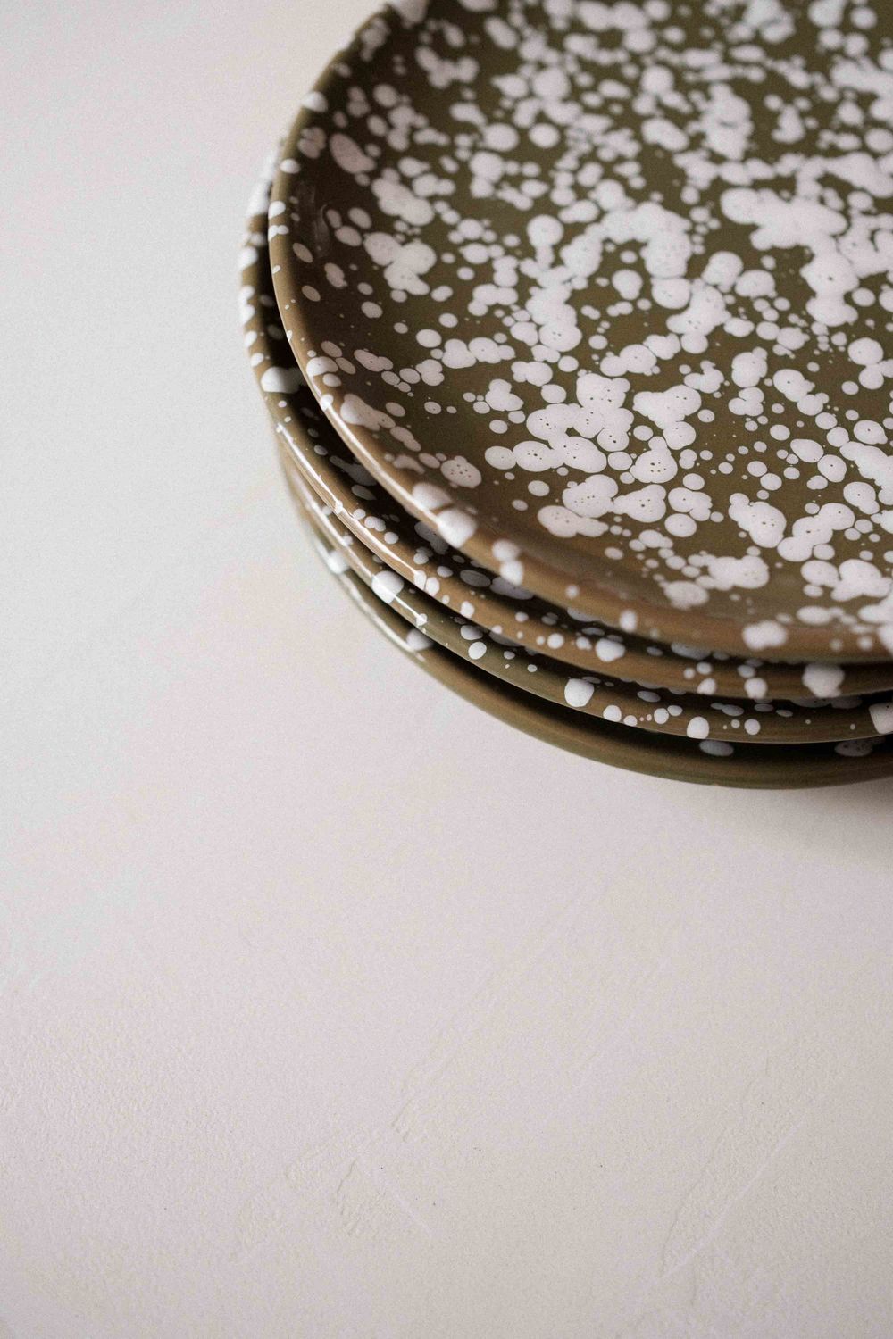 Stack of speckled ceramic plates with white and olive green pattern on light surface.
