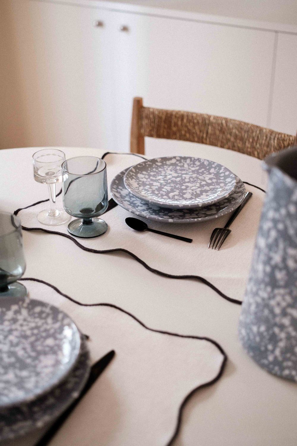 Dining table with gray speckled plates and smoky glassware on white tablecloth.