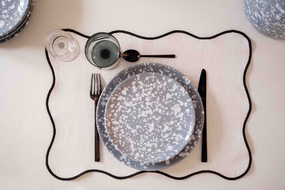 Overhead view of modern place setting with speckled plate and black wavy placemat outline.