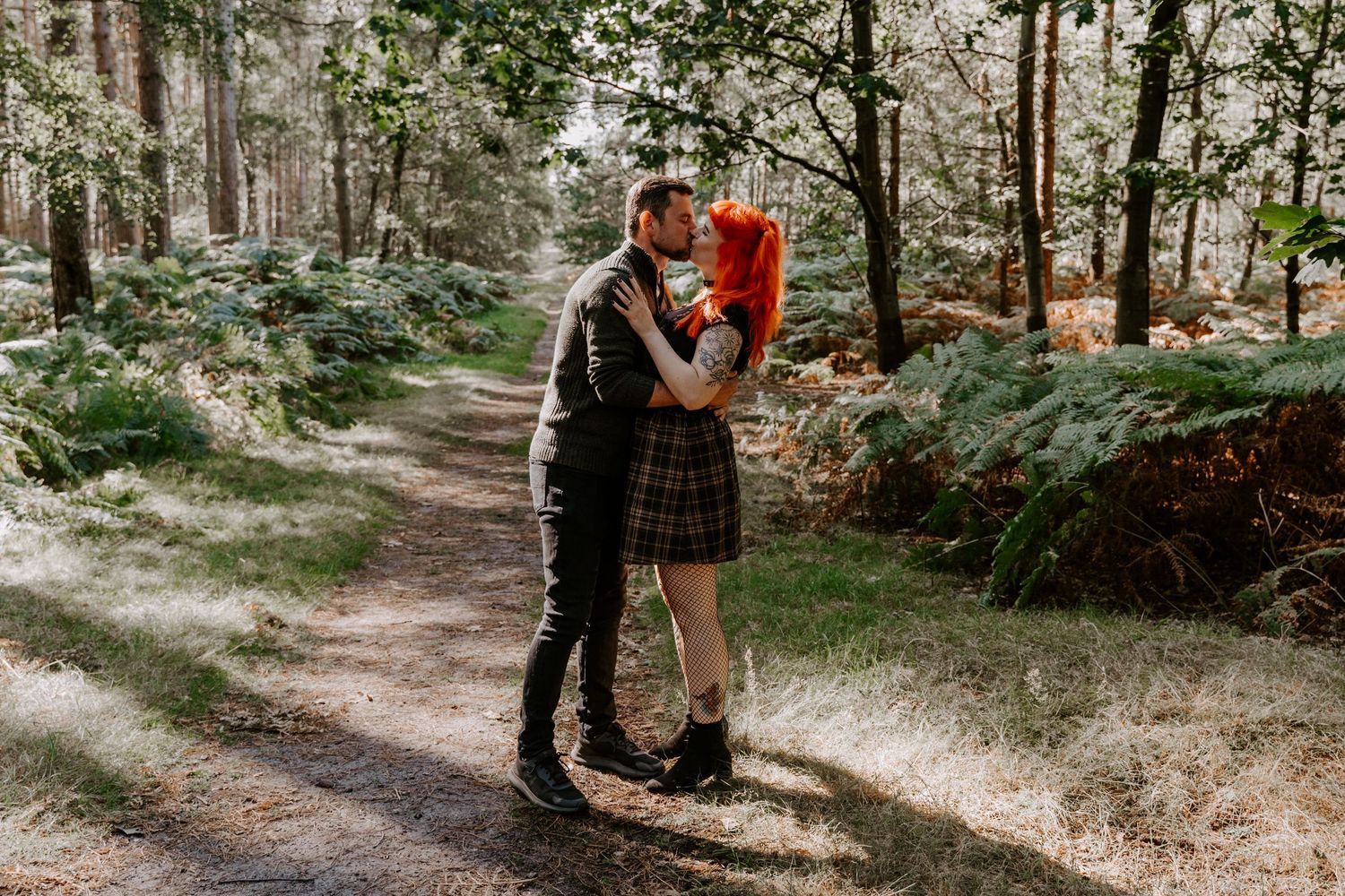 A couple are stood in the middle of Sandringham woods, Norfolk. They are standing face to face and are kissing.