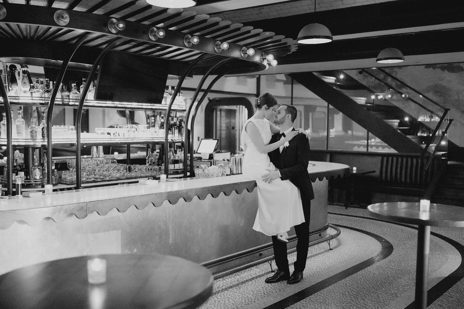 Bride and groom share a tender kiss at a stylish bar venue in a romantic black and white photo.