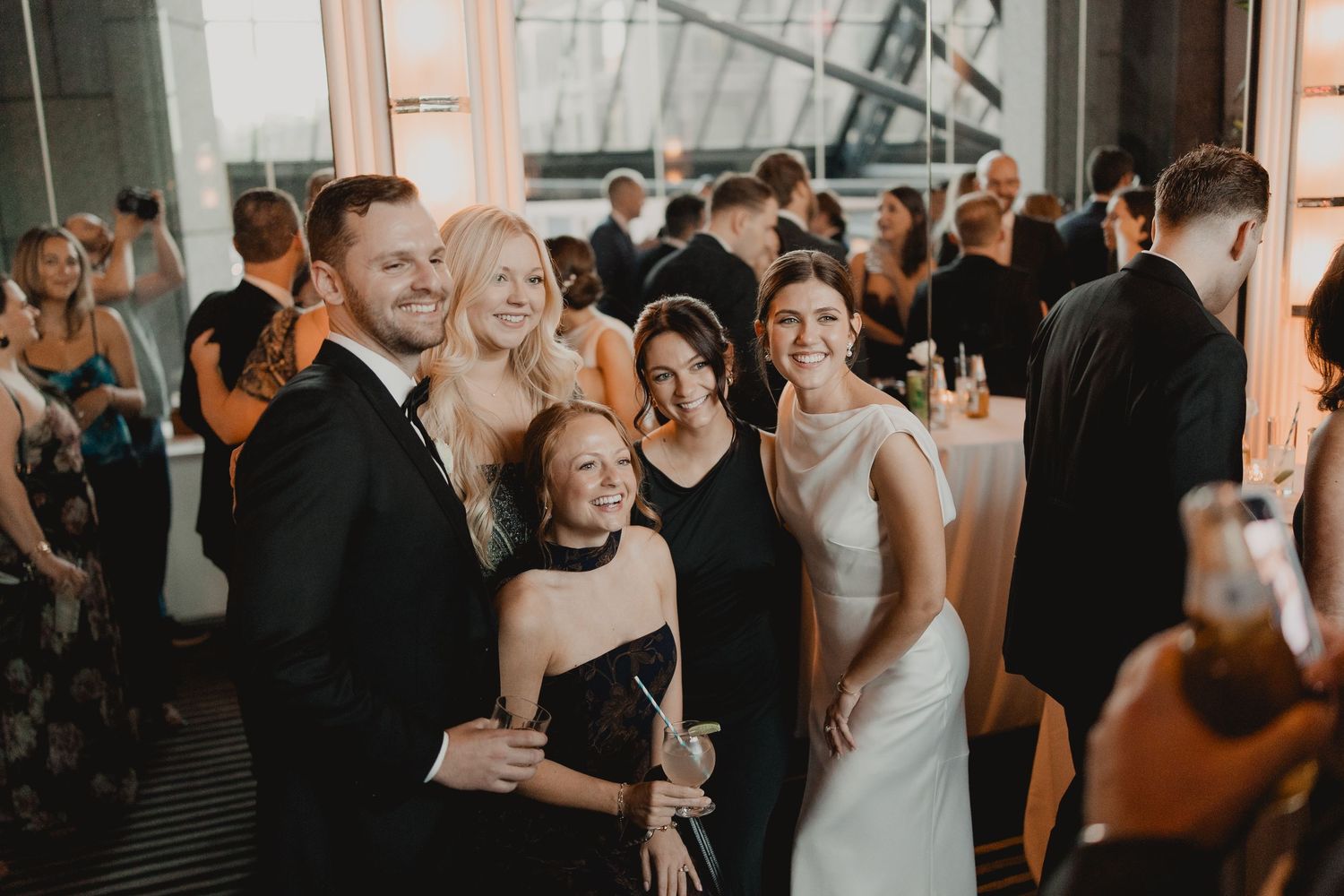 Wedding guests smile for a group photo at an elegant indoor reception venue during a formal celebration.