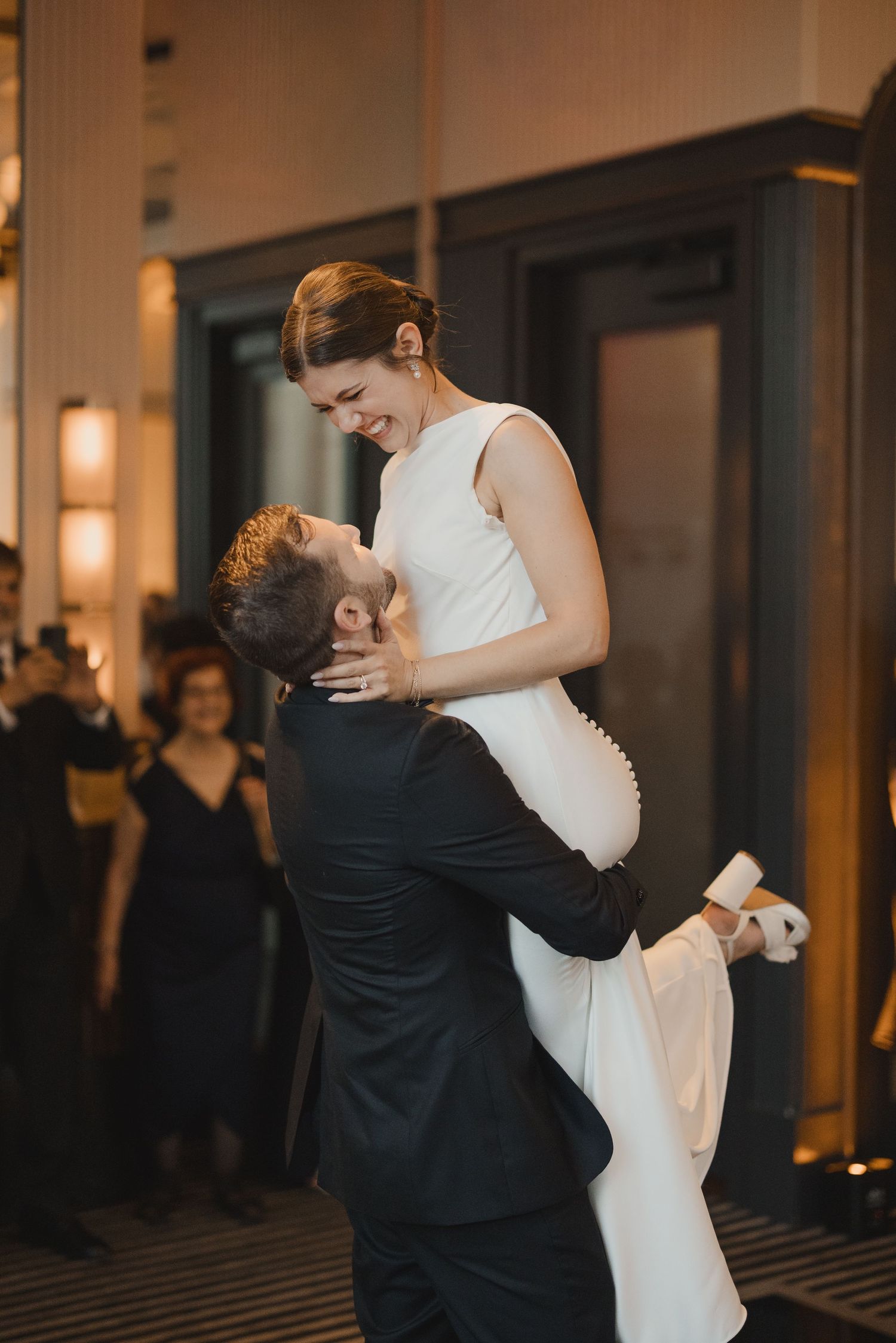 Groom lifts smiling bride during their first dance at an elegant indoor wedding reception venue.