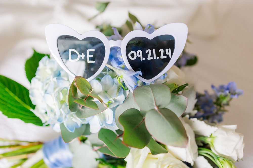 Heart-shaped sunglasses with wedding date decorated with blue and white floral arrangements.