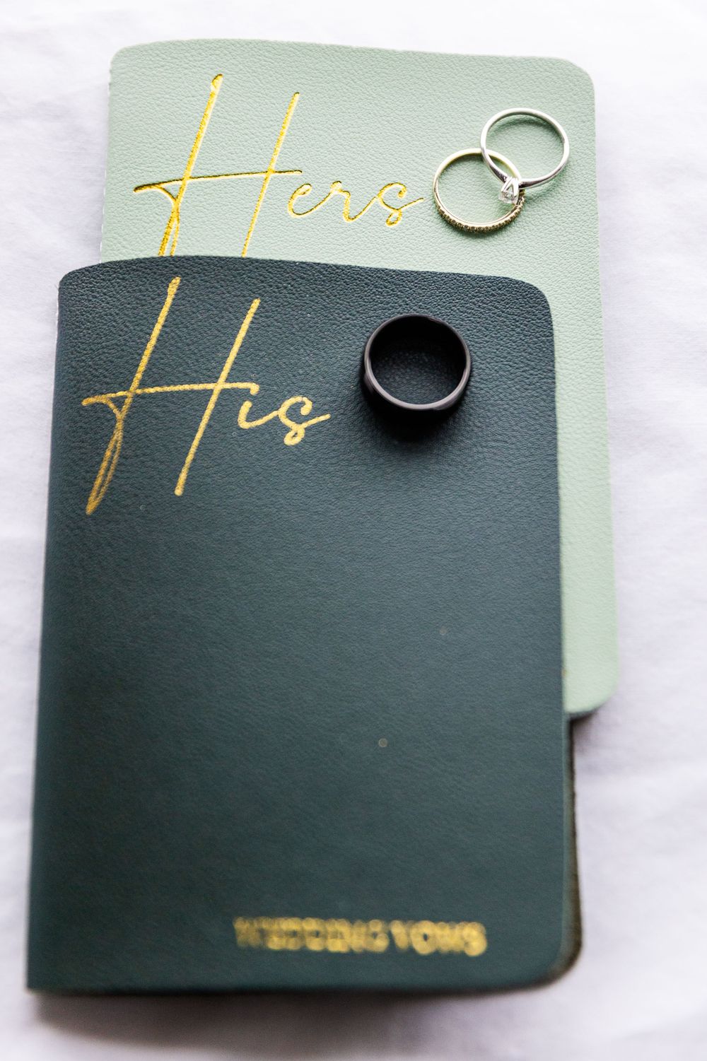 His and Hers wedding vow books with wedding rings displayed on white surface.