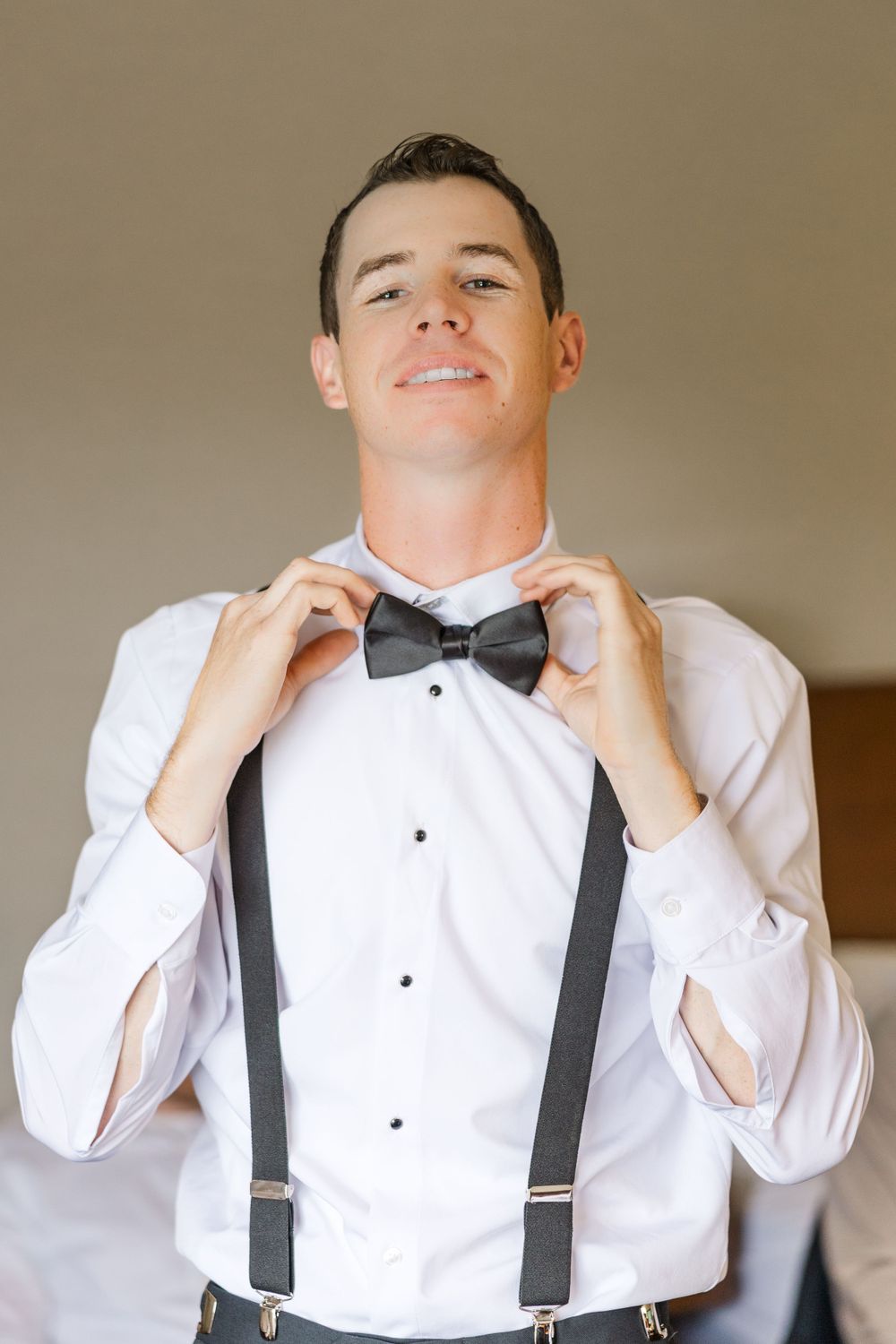 Person in formal attire adjusting black bow tie and suspenders.
