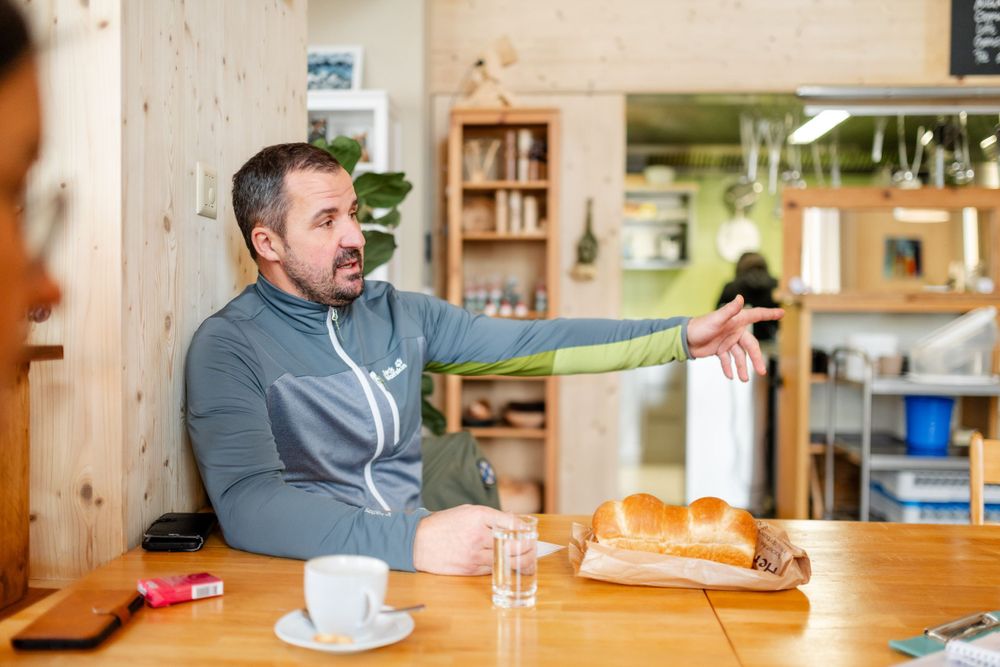 Person in grey sweater gesturing while sitting at casual dining table.