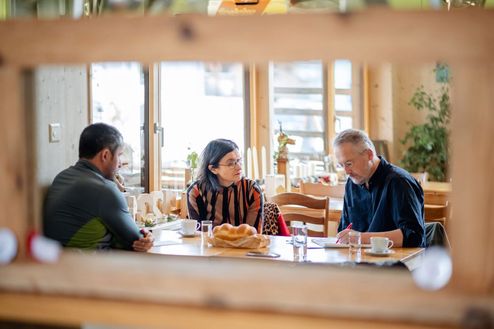 Three people having casual conversation over meal at cafe table.