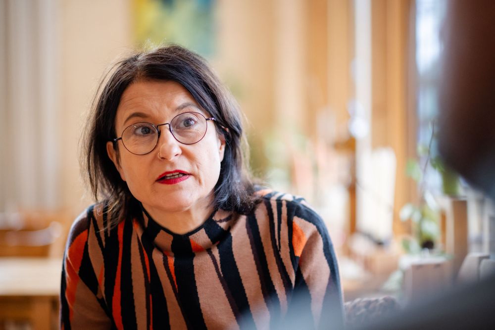 Person in striped shirt and glasses seated in a bright interior space.