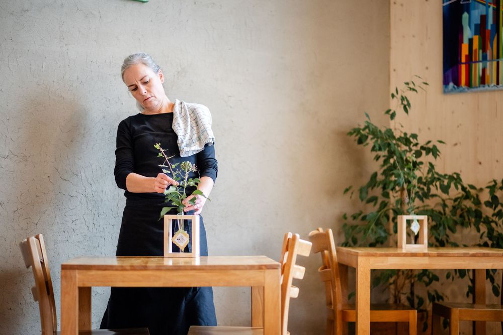 Person in dark apron arranging flowers at a wooden table with decor.