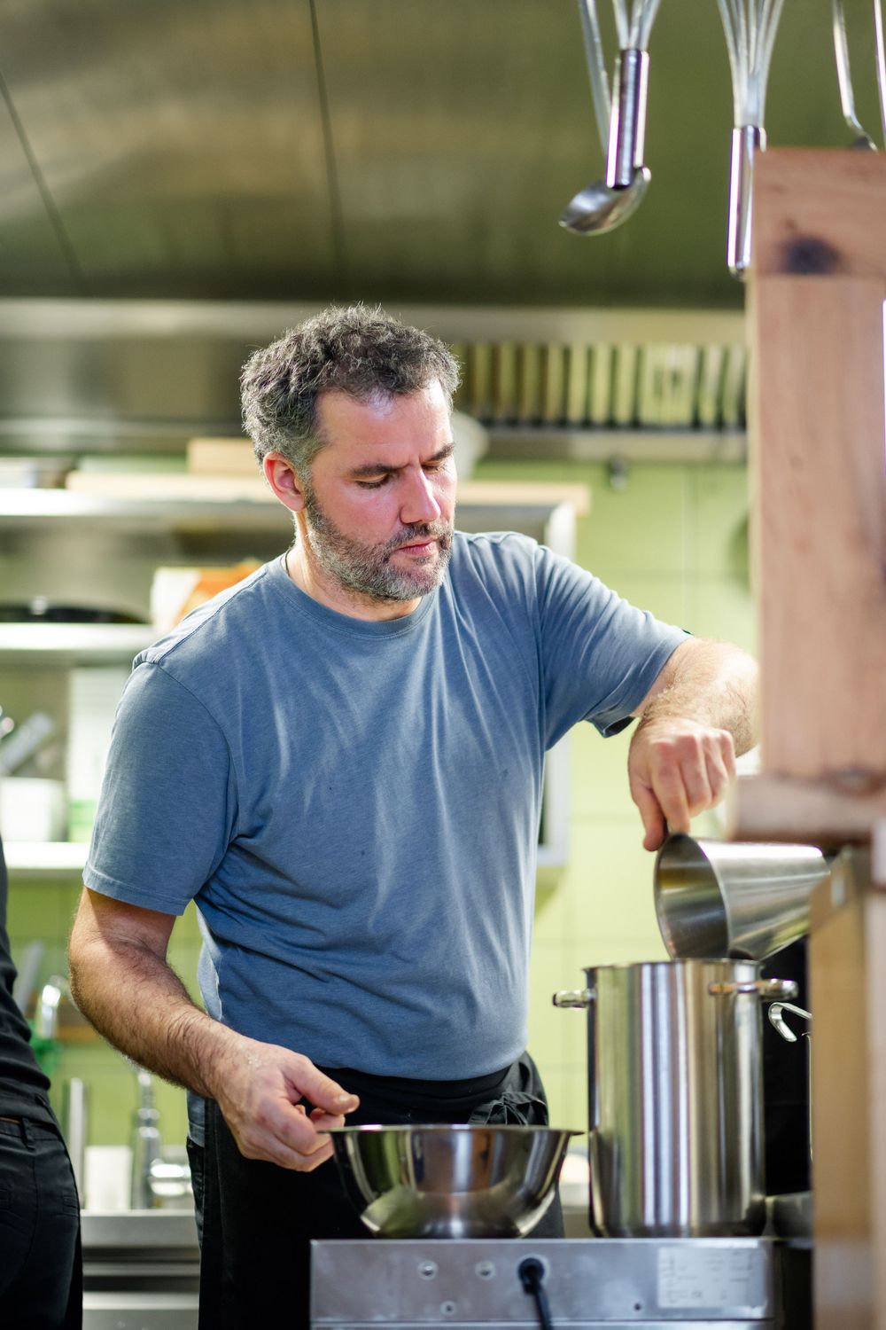 Chef in blue t-shirt working at a commercial stove in a restaurant kitchen.