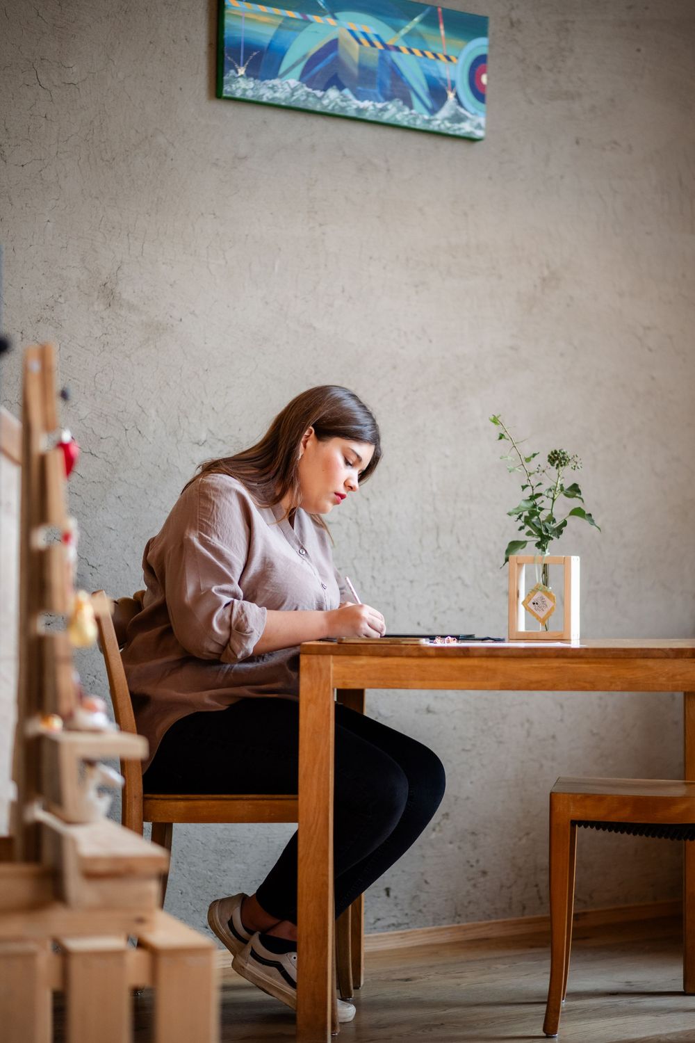 Person in beige sweater writing at wooden table with decorative elements nearby.