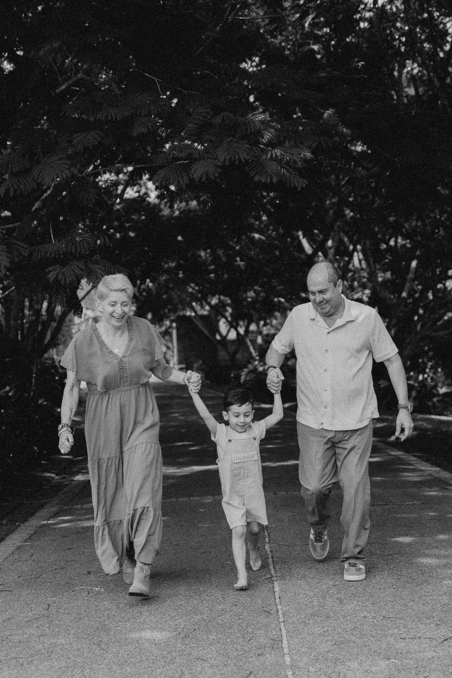 A joyful family moment as they swing and play together on a sidewalk near greenery.