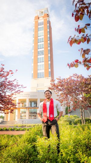 A bright yellow field of flowers blooms in front of a modern brick university building with red autumn leaves overhead.