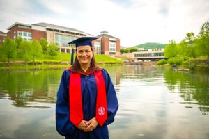 Graduation photos taken by a lake with academic regalia and campus buildings in background.