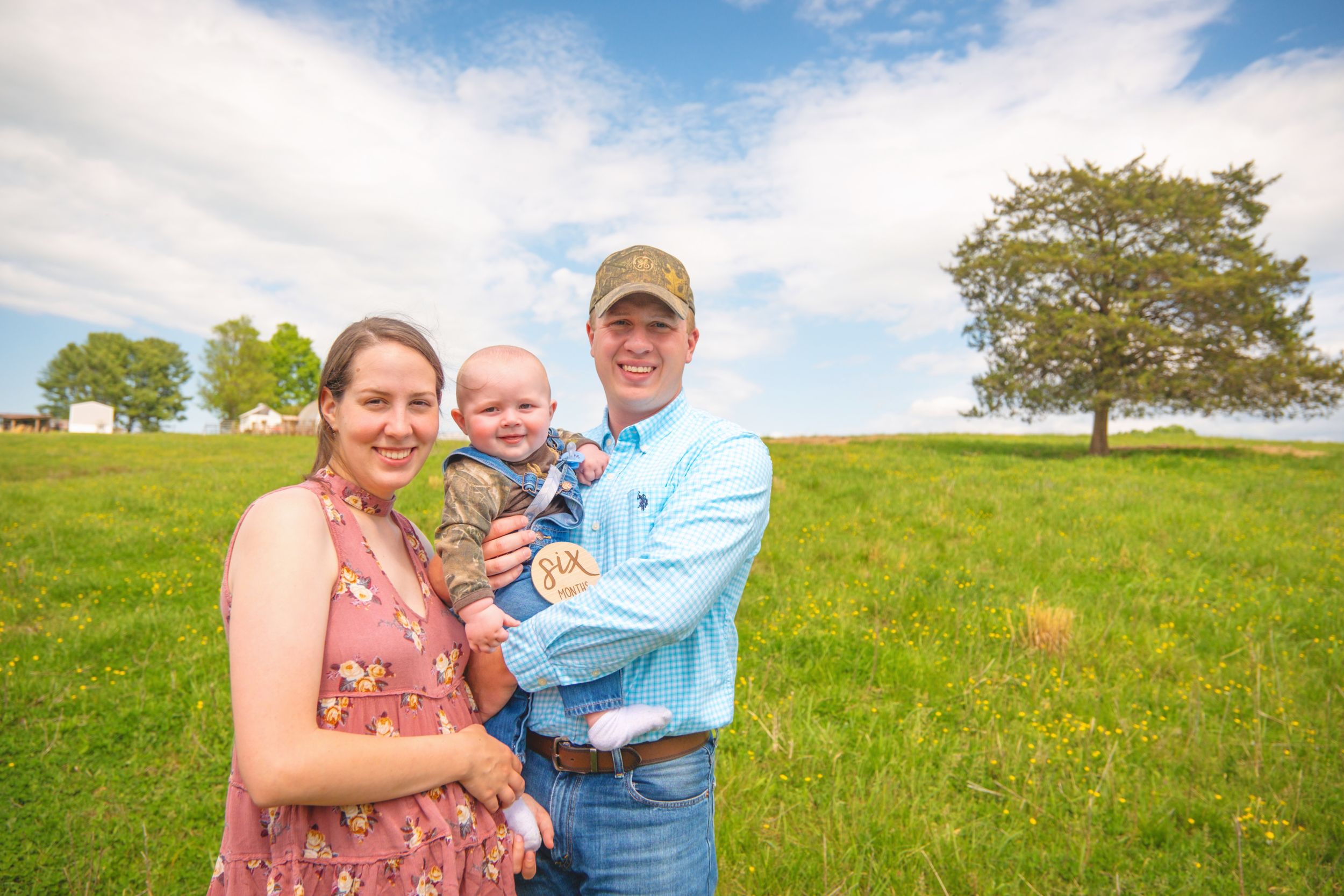 Family gathering on a grassy hillside with trees on a bright sunny day.