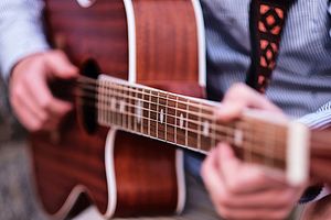 Close-up view of hands playing an acoustic guitar with wooden fretboard and strings in focus.