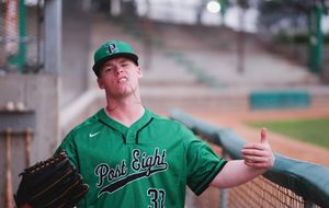 Baseball players in green jerseys sit and stand in a dugout during a game.