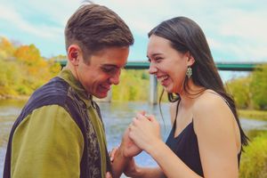 A couple laughs together while sharing a joyful moment outdoors with autumn foliage in the background.