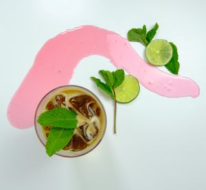 Four progressive shots showing a pink cocktail being poured into a glass with mint and lime garnish.