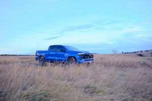 A bright blue Ford pickup truck parked in a golden prairie field under clear blue skies.