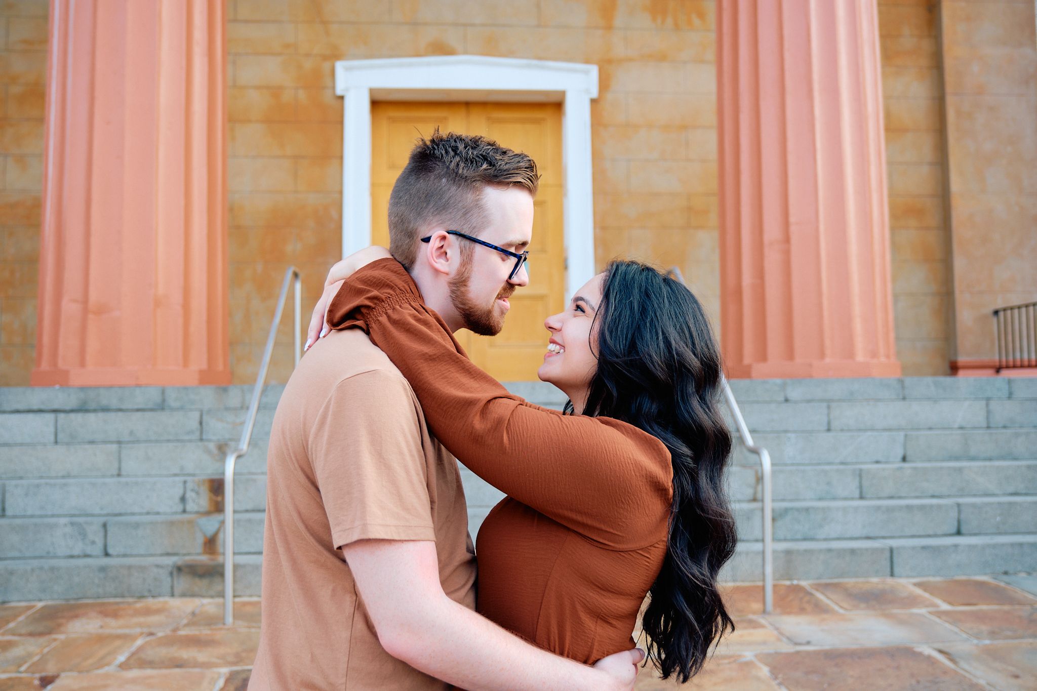 A couple shares intimate moments in a series of photos against a brick wall with pink-tinted columns.