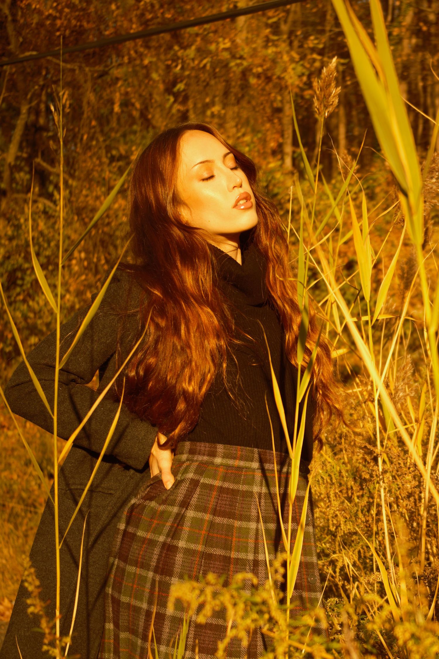 A warm-toned portrait of someone in plaid skirt amidst golden grasses at sunset.