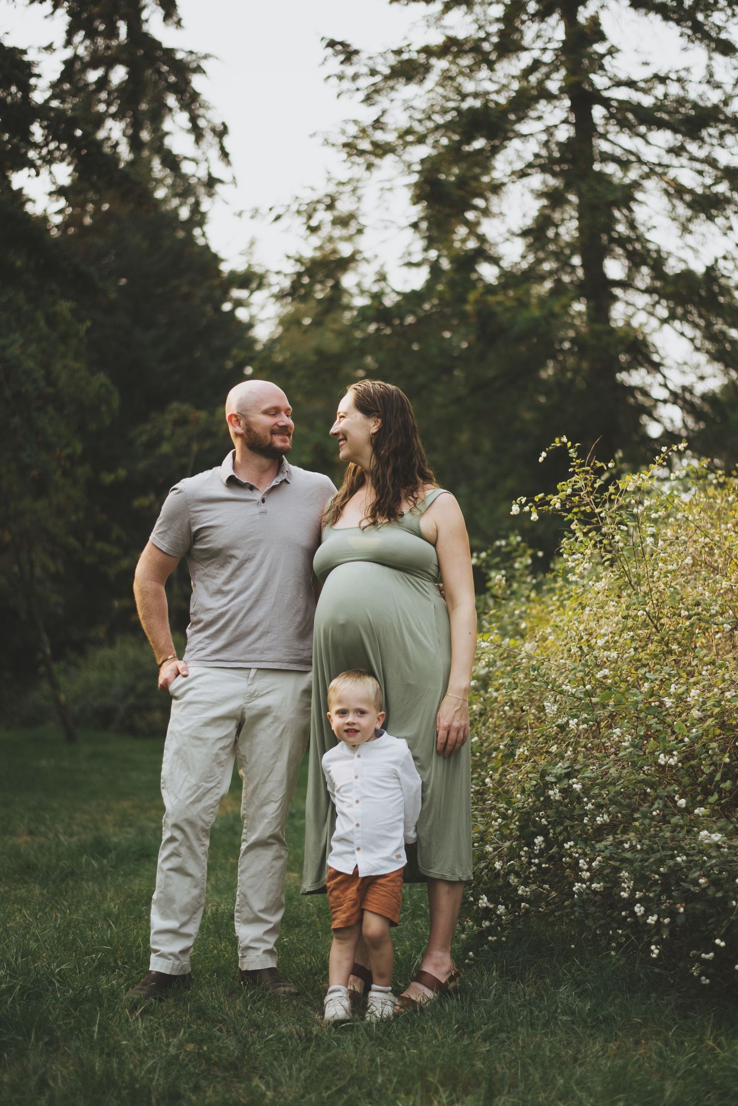 A family stands together in a sunlit meadow with evergreen trees in the background.