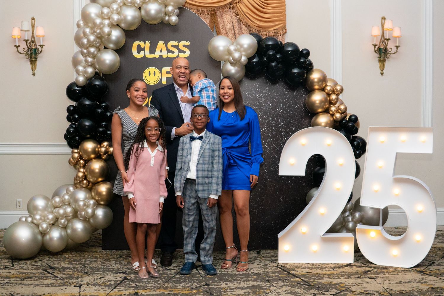 Family of five posing together at a Class of 25 graduation celebration with balloon arch backdrop.