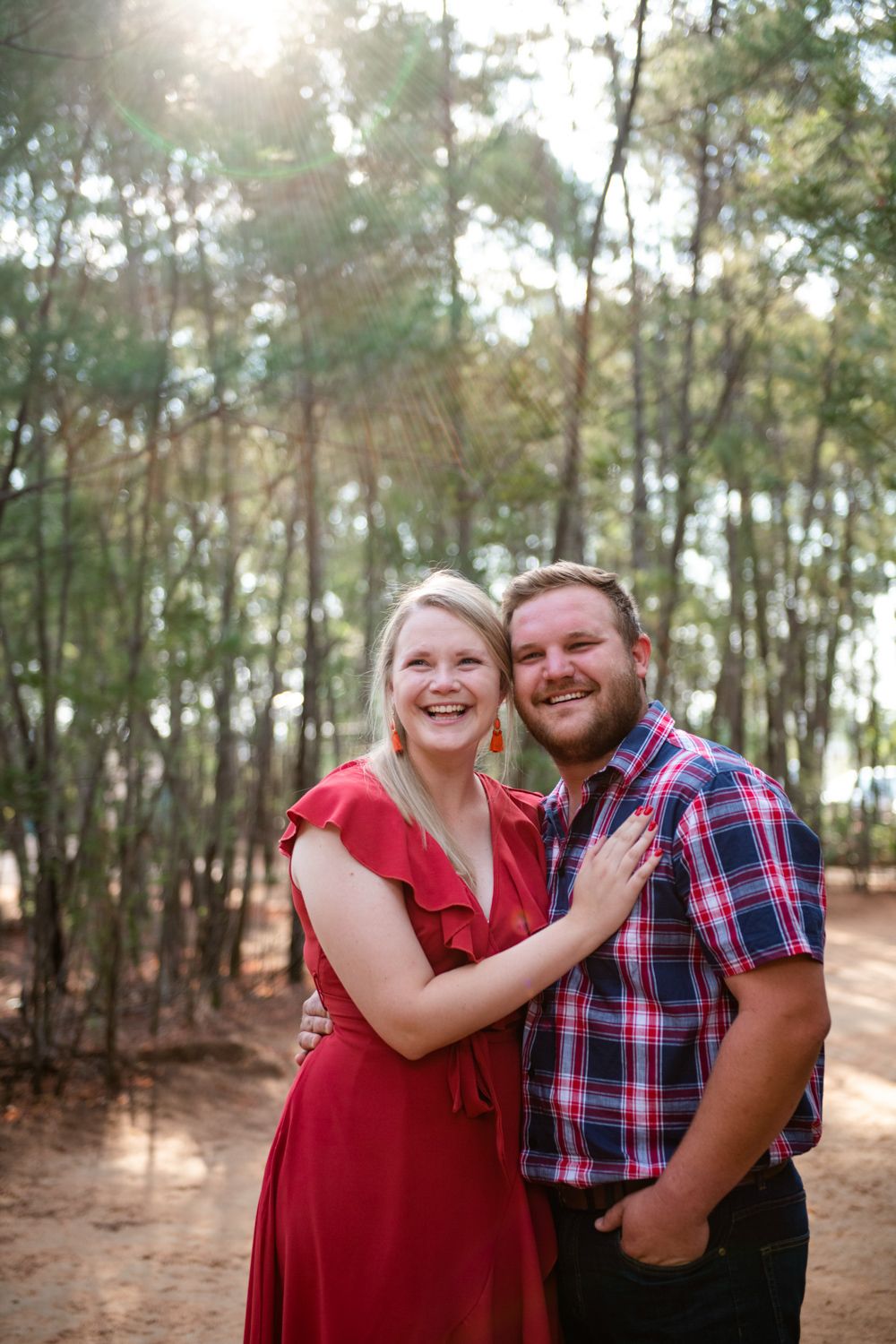 Romantic portrait of an engaged couple backlit by the sun in a forest setting.