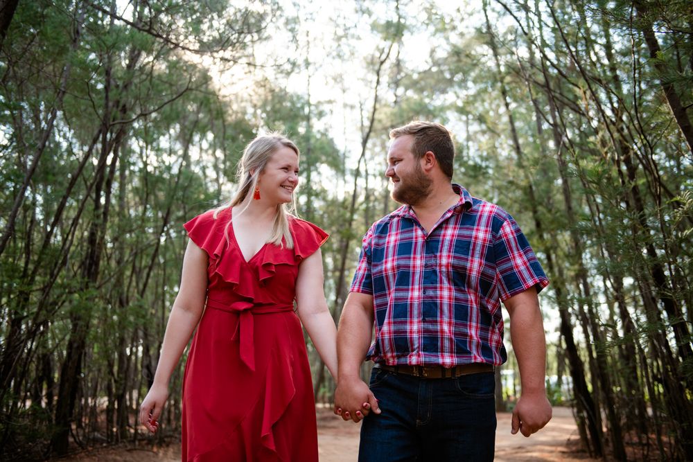 Loving couple walking hand-in-hand through a pine forest during their engagement shoot.