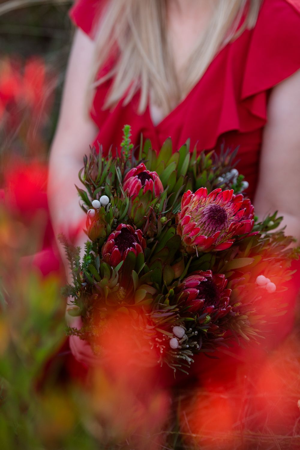 Close-up detail of the engagement ring and red dress amongst the red flowers.