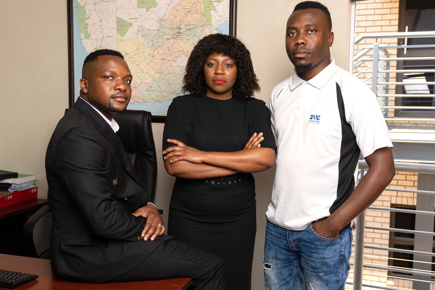Three professionals in business attire pose together in an office setting with a map visible in the background.