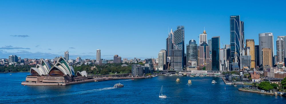 Panoramic view of Sydney Harbour with the iconic Opera House, CBD skyline, and blue waters under a clear sky.