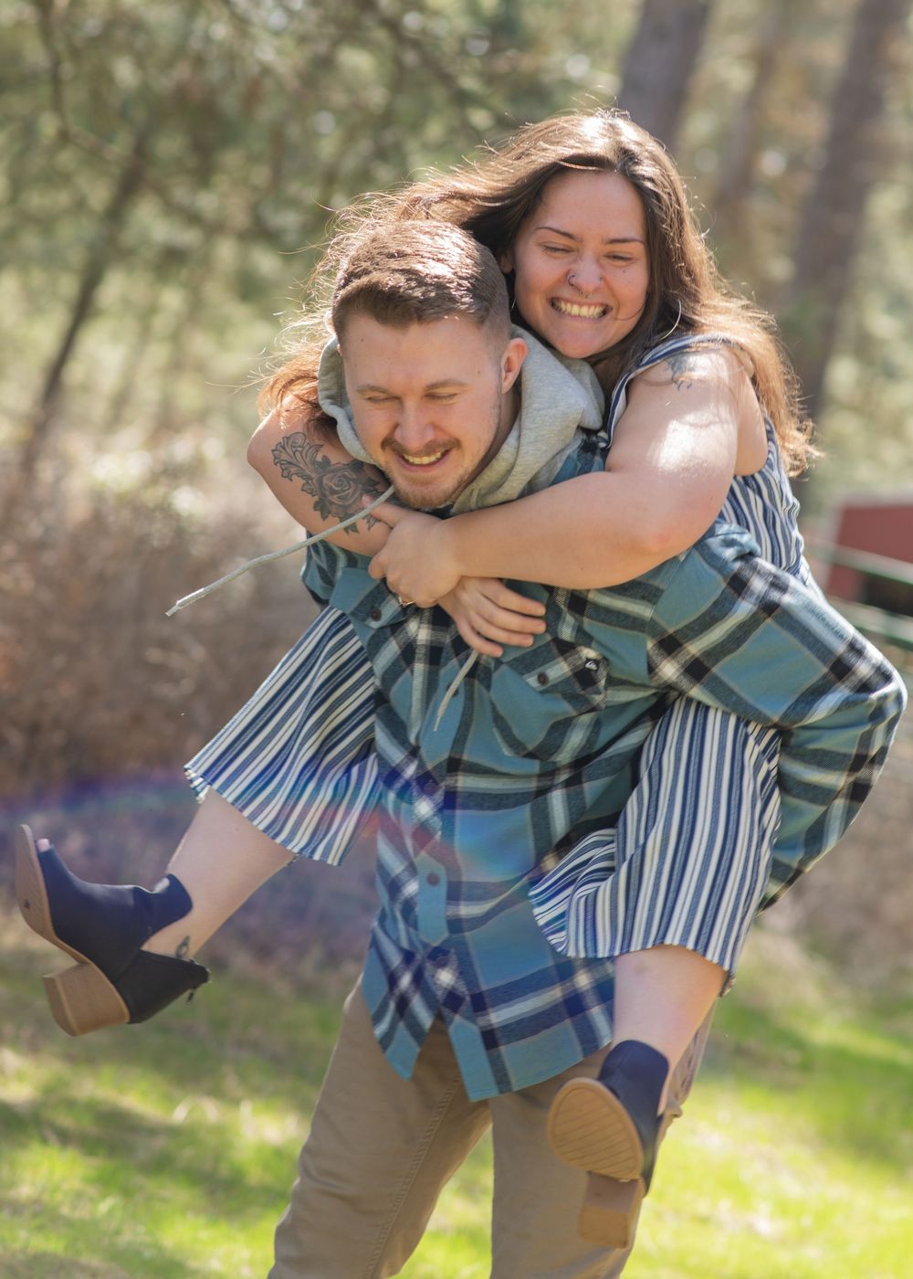 A joyful couple laughs as the man gives the woman a piggyback ride in a sunny park.