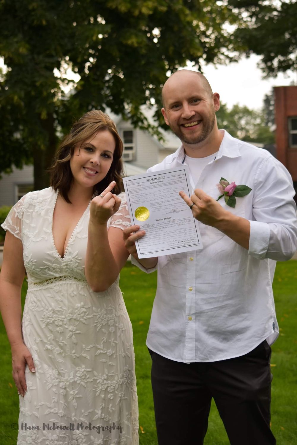 Newlyweds proudly display their marriage certificate outdoors after their wedding ceremony.