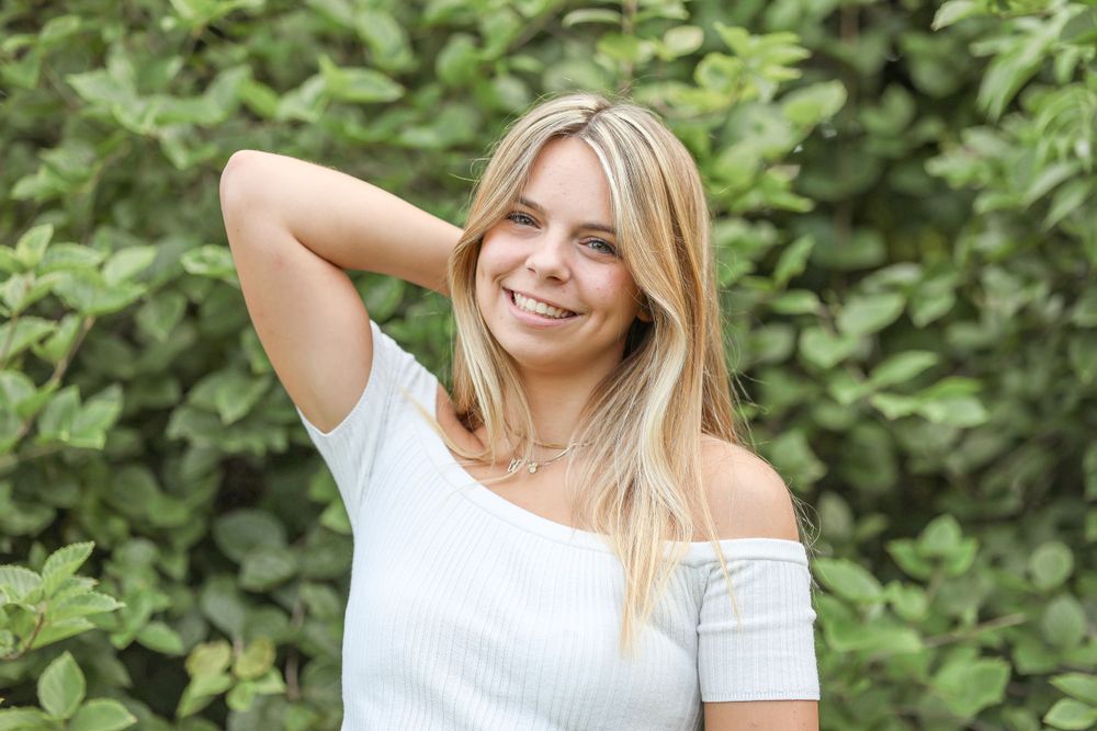 A relaxed outdoor portrait against green foliage in summer attire.