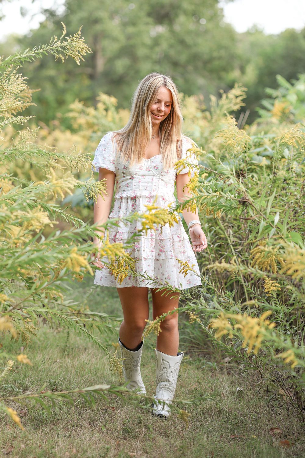 A delicate floral white dress paired with matching knee-high boots amidst golden wildflowers in a natural setting.