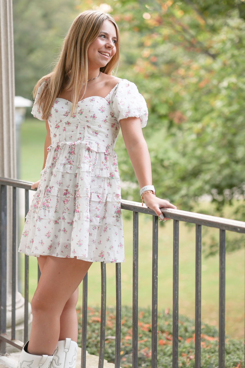 White puff-sleeve dress styled with boots while posing on an outdoor balcony railing.