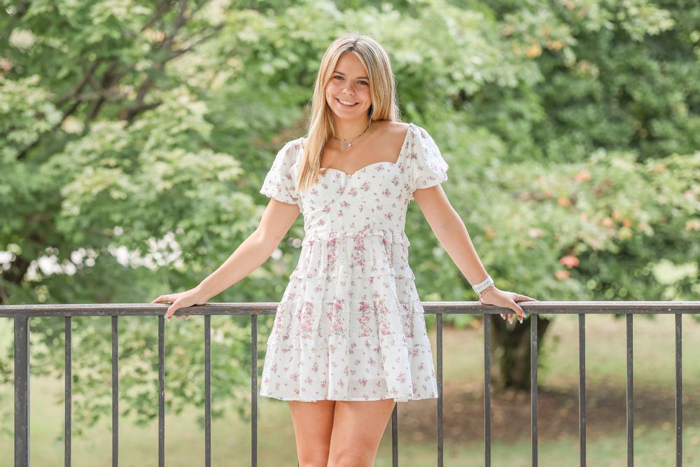 Summer fashion pose in a white floral dress against a wrought iron balcony.