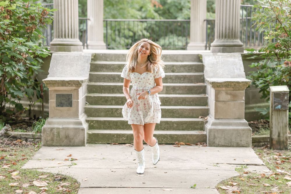 White floral dress and boots styled against grand stone steps and columns in an outdoor setting.