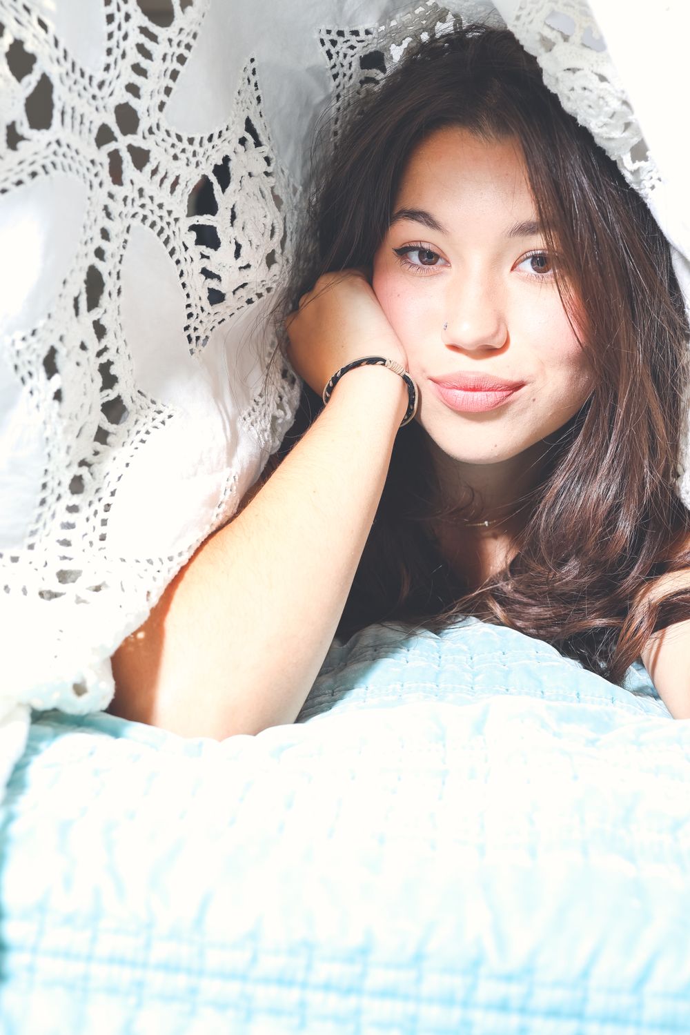 A soft portrait against white lace curtains with natural lighting.