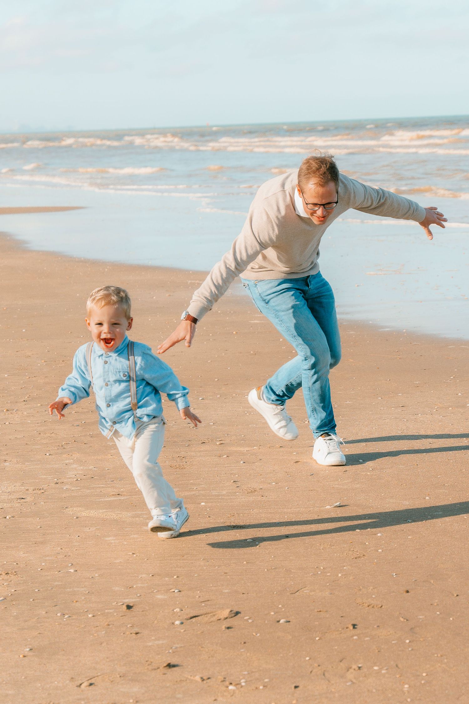 Two people running and playing together on a sandy beach with ocean waves in the background.