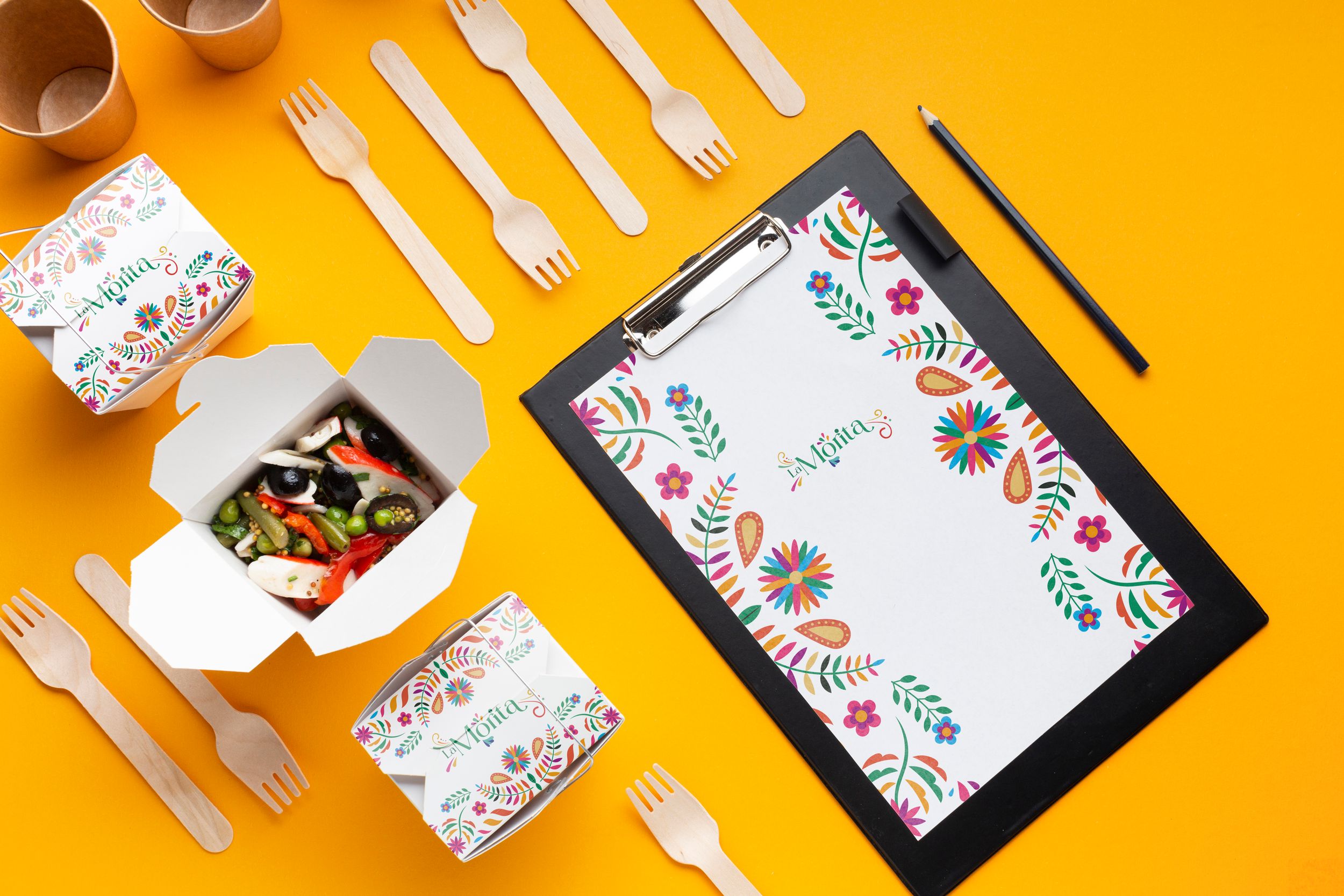 Overhead view of eco-friendly dining set with floral patterned clipboard on orange background.