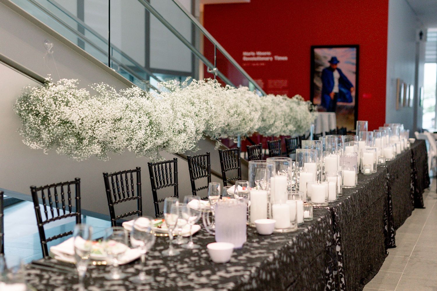 An elegant long dining table set with white flowers, candles and dark chairs in a modern event space.