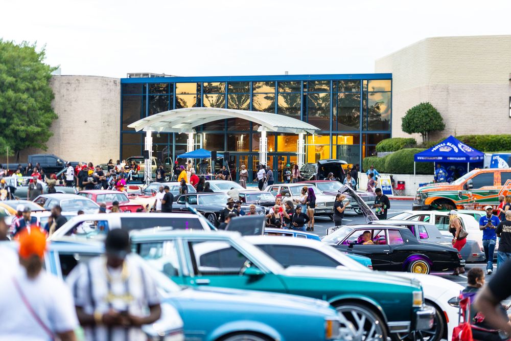 Aerial view of car show gathering with vintage vehicles and large crowd in parking lot. | Shot By Lo™