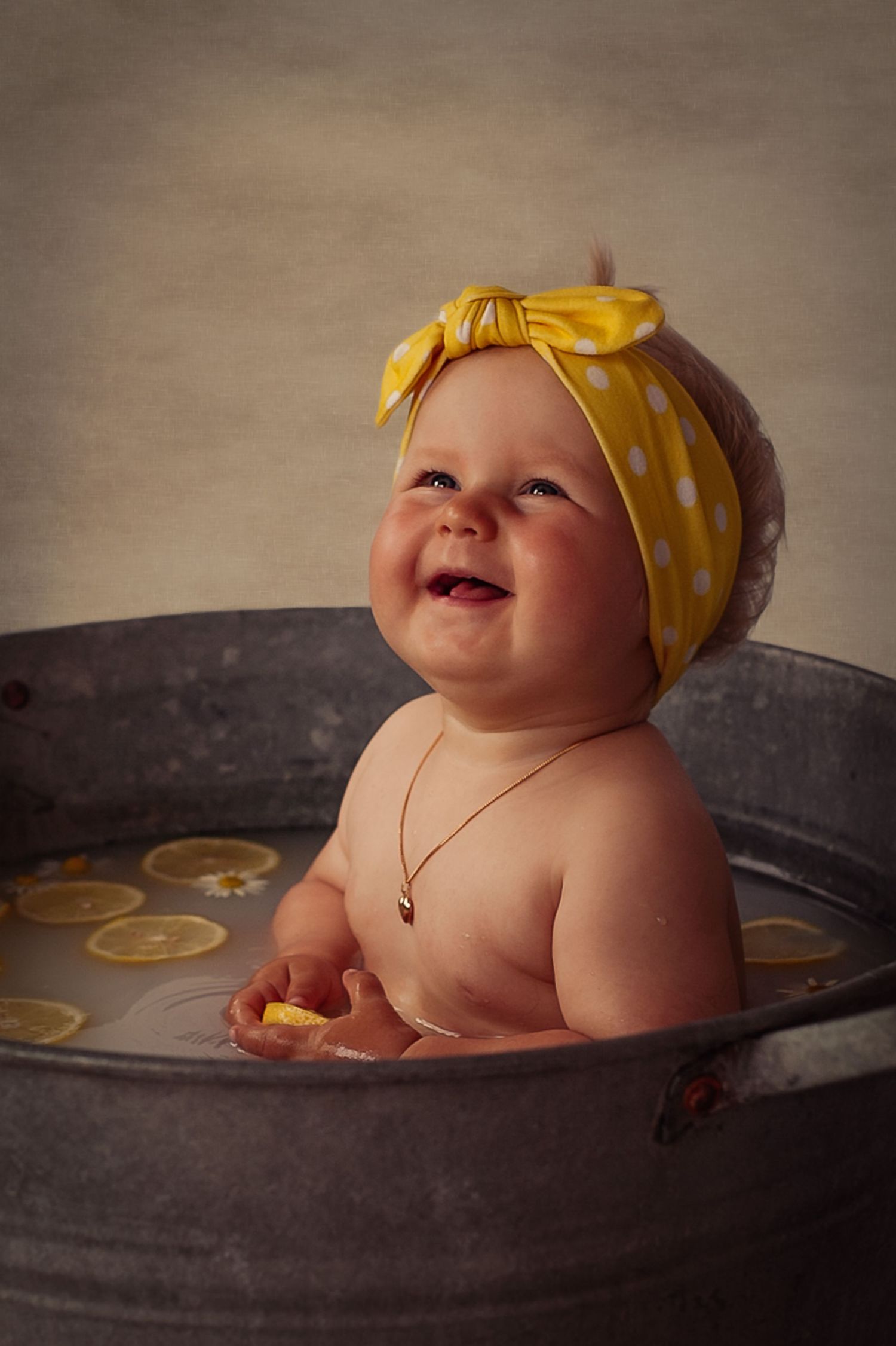 Vintagebild. Mjölkbad. En liten flicka sitter i en gammal zinkbalja. I mölkbadet är det citronskivor och vita blommor.